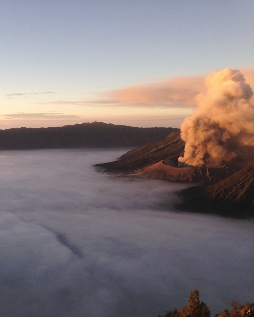 A smoking volcano above a sea of cloud at sunrise